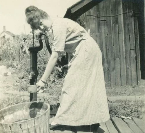 Woman pumping water from a hand well, vintage photo